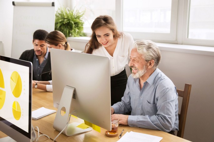 Smiling young manager helping senior worker with computer office